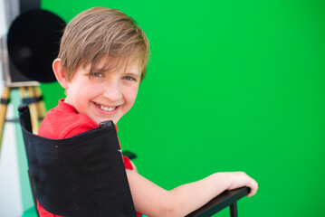 boy is sitting in the director's chair on a green background. a child on the set, migrating to the...