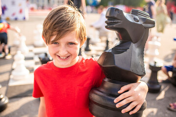 smiling boy hugging a knight chess piece. happy little chess player, child, playing street chess...
