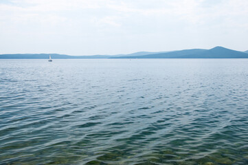 Landscape view of Turgoyak lake with a sailboat in the background, South Ural, Russia