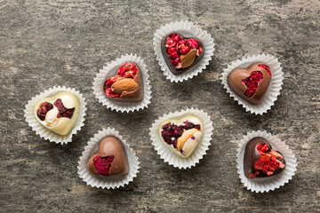 chocolate sweets in the form of a heart with fruits and nuts on a colored background. top view with space for text, holiday concept