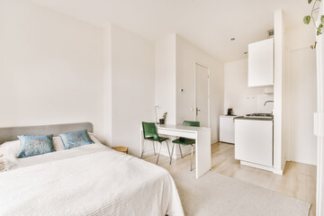 a bedroom with a bed, desk and small kitchen in the room next to the bed is a white refrigerator