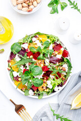 Beetroot and white cheese salad with arugula, lettuce,  orange and pistachios on white table. Fresh useful dish for healthy eating