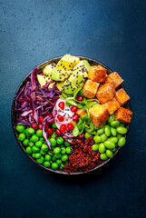 Vegan buddha bowl with red quinoa, fried tofu, avocado, edamame beans, green peas, radish, cabbage,...