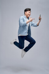 Excited man holding and pointing finger at his cellphone while jumping isolated over white background
