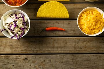 Directly above shot of cheese and cabbage in bowls with tortillas and chili on wooden table