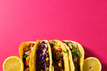 Directly above shot of tacos with lemon slices against pink background, copy space