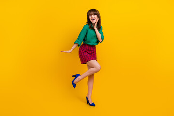 Fototapeta na wymiar Full size photo of cheerful stunning young girl hand touch cheek stand one leg good mood isolated on yellow color background