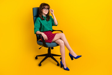 Full length portrait of lovely pretty person sitting office chair hand touch eyeglasses isolated on yellow color background