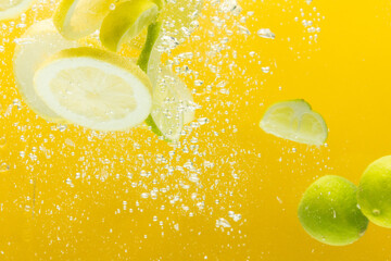 Close up of lemon and lime slices falling into water with copy space on yellow background