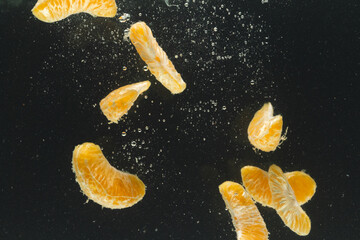 Close up of tangerine segments falling into water with copy space on black background