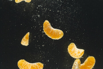 Close up of tangerine segments falling into water with copy space on black background