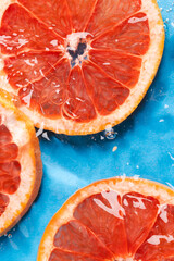 Close up of red grapefruit slices in water with copy space on blue background