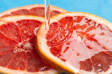 Close up of red grapefruit slices in water with copy space on blue background