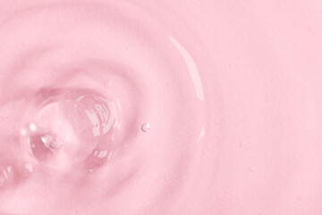 Close up of water drop falling into water with ripples and copy space on pink background