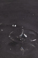 Close up of water drop falling into water with ripples and copy space on black background