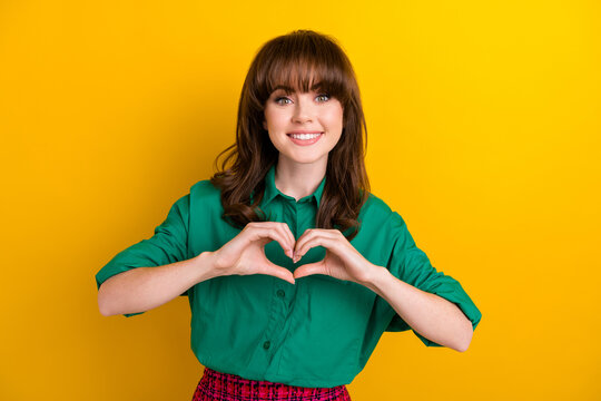 Photo of funky cheerful woman dressed green shirt showing arms fingers heart isolated yellow color background