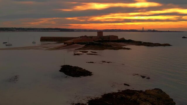 Aerial Drone slow pull back from St Aubin's Fort in the town of St Aubin, Jersey, Channel Islands at sunset