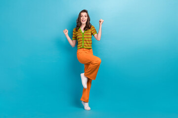 Fototapeta na wymiar Full length photo of nice pretty impressed girl wear striped shirt trousers raising fists win lottery isolated on blue color background