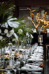 Luxuriously set wedding table, vases with white flowers and fern leaves on the table, food and drinks. Side view.