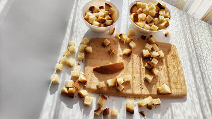 Homemade slices of diced dry white rye bread on cutting board and white plate. Crackers for food, healthy eating on table in sunny day, top view