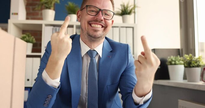 Young smiling businessman sitting at table and showing middle finger 4k movie. Bad business deal concept