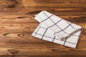 Kitchen towel on a brown wooden background. Kitchen utensils and textile napkin. A stack of cotton towels on the table. Home decor. Tablecloth for the table. Copy space for text. Mockup for design.