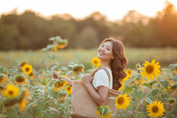 Beautiful young Asian woman in sunflower field at sunset. Model with dark long curly hair. Summer, sun.