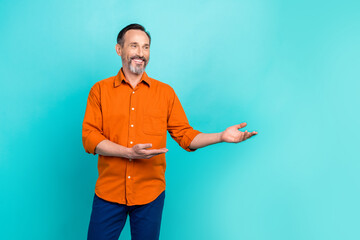 Photo of retired entrepreneur wear orange shirt hands holding looking empty space brand company ad isolated on cyan color background