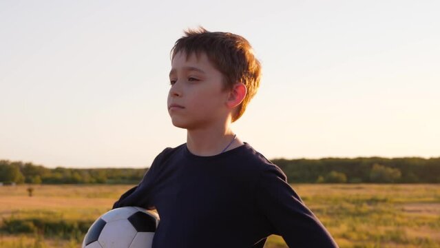 Portrait of a boy against the sunset. A child soccer player holds the ball. Kids dreams, kids in sports
