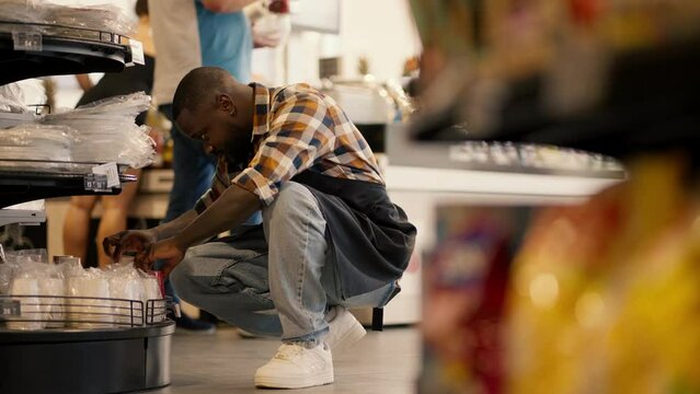 a man with Black skin color in a plaid shirt and a black apron sorts disposable tableware on a supermarket counter