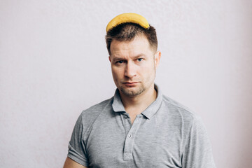 A guy in a gray t-shirt holds a yellow banana on his head
