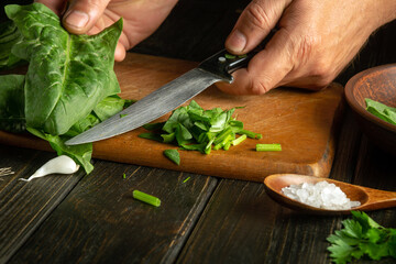 The cook prepares a salad with fresh vegetables and spinach. The concept of cooking vegetarian food on the kitchen table