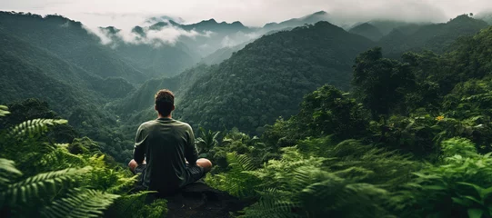  Back view of a sitting man observing the hills covered with rainforest, low clouds © Aleksandr Bryliaev