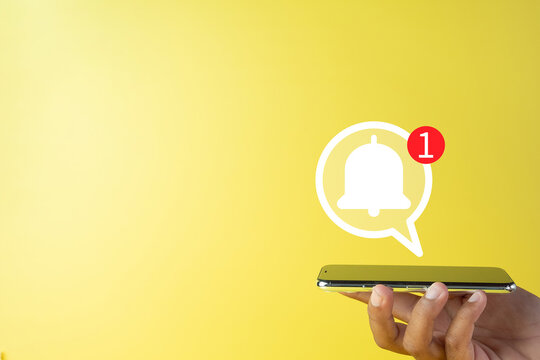Social media,notification ,reminder,,incoming message concept.,Hand holding smartphone with Message bell and speech bubble icon over yellow background with copyspace use for technology idea.