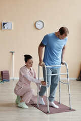 Vertical image of patient trying to walk with walker and doctor helping him during his rehabilitation