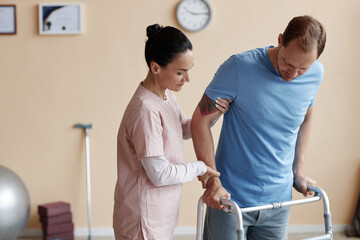 Fototapeta premium Doctor helping patient to walk with walker during his rehabilitation in hospital