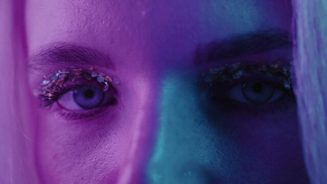 Fashion model face woman in colorful bright neon, uv blue and purple lights, beautiful girl, glowing make-up, colorful. Glitter Vivid neon makeup. Close up female portrait opening eyes
