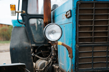 Close-up of a retro blue old farm tractor outdoors, selective focus on a round headlight