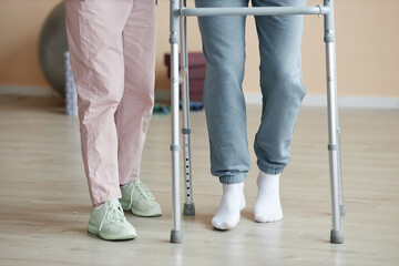Close-up of patient learning to walk with walker together with doctor helping him