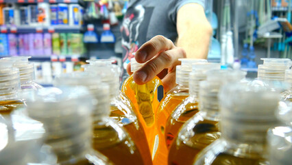 Close-up of many detergent bottles on a store shelf and a male buyer takes one