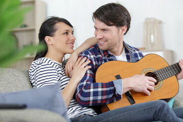 Fototapeta premium couple snuggled on the sofa while the man plays guitar