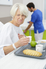 Fototapeta na wymiar nurse serving unappetizing diet dinner to old woman in bed