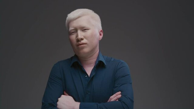 Portrait of an Asian albino guy. Eastern man with a genetic mutation of pigment, white hair. The arms are crossed on the chest. The male is wearing a dark shirt in the studio. Abnormal deviations