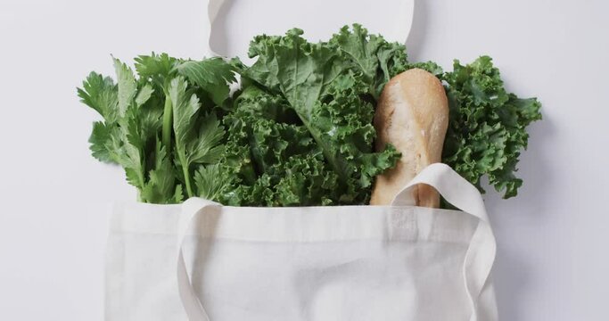Video of white canvas bag with parsley, kale and baguette, copy space on white background