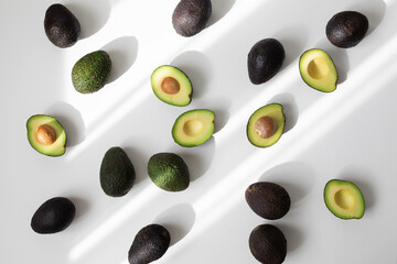 Heap of ripe whole and half avocados on white background top view in aesthetic shadow sunlight....