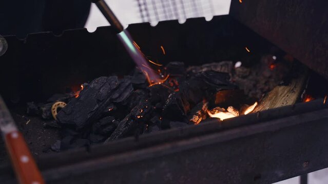A man kindles coals in a brazier for cooking with a gas burner. Close-up of hands and burner.