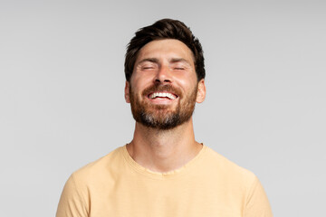Happy bearded man model posing with closed eyes isolated on gray background. Confident modern hipster with stylish hair enjoying success