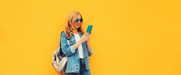 Portrait of stylish modern smiling young woman with phone wearing jean jacket on yellow background