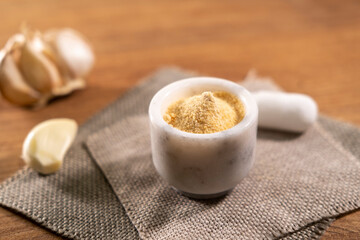 Ground dried garlic in small bowl and cloves on wooden background, spice garlic
