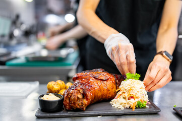 chef hand cooking Baked Pork knuckle with vegetables on plate in kitchen